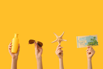 Sticker - Female hands with sunscreen, sunglasses, starfish and travel gift voucher on yellow background. Travel concept.