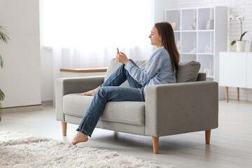 Wall Mural - Young pretty woman chatting with mobile phone on couch at home
