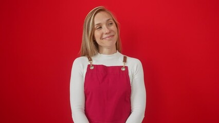 Poster - Cheerful young blonde woman in apron, lost in thought, casting interested sidelong glances, smiling brightly against vibrant red isolated background.