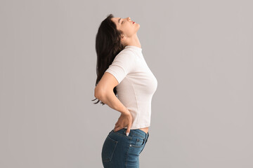 Wall Mural - Beautiful young woman suffering from back pain on grey background