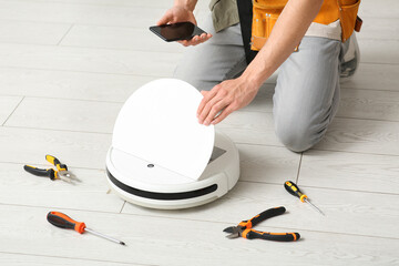 Man with tools and mobile phone fixing modern robot vacuum cleaner at home