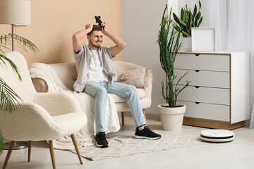 Sticker - Young man playing video games with modern robot vacuum cleaner at home