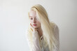 © XaMaps - Albino woman dressed in white on a white background, lost in thought.