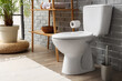 © Pixel-Shot - Interior of restroom with toilet bowl, plant and shelving unit near grey brick wall
