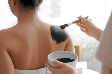 Wall Mural - Massage therapist applying mud on woman's back in spa salon, closeup