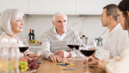 Wall Mural - Senior man and woman play card game poker during friendly gatherings at home with middle-aged couple. Couple enthusiastically participate in game, believe in luck, collect chips, distribute winnings