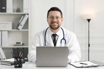 Wall Mural - Smiling doctor with laptop at table in clinic. Online consultation