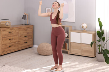 Poster - Happy woman standing on floor scale at home