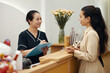 © DragonImages - Spa salon cosmetologist talking to client filling form with personal data