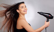 © Alexis S/peopleimages.com - Portrait, happy woman and hairdryer in studio for beauty, wellness and cosmetics. Model girl, smile or face and wind for salon treatment, glow and shine with results for hair by white background