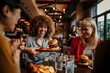 © La Famiglia - Waiter serving burger to a group of friends having lunch at a restaurant - food service concepts