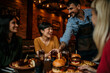 © La Famiglia - Waiter Serving Group Of Female Friends Meeting For Drinks And Food In Restaurant