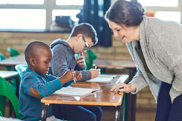 Poster - Teacher, woman and help child writing in notebook for education, study or knowledge in class. Kid, happy educator and student learning in lesson for development or assistance at kindergarten school