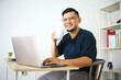 © Gatot - Asian man enjoy drinking coffee while working on laptop at home office. Remote job concept.
