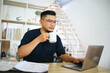 © Gatot - Asian man enjoy drinking coffee while working on laptop at home office. Remote job concept.