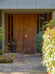 Poster - A contemporary design house entrance with a wooden door between lush foliage. Travel to Athens, Greece.