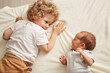 © sementsova321 - Happy toddler with her brother. Caucasian siblings at home. Cute brother and sister moments. Curious wavy haired older sister with newborn baby