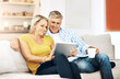 © MollerFinest/peopleimages.com - Relax, tablet and mature couple on couch with coffee, smile and scroll on social media together in home. Bonding, man and woman on sofa with digital app for streaming, reading and online connection.