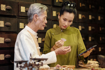 Wall Mural - Young woman helping her dad in drug store, she using tablet pc to examine herbs