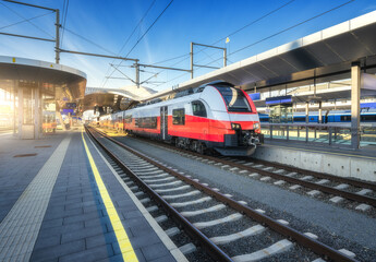 Wall Mural - high-speed red passenger train at railway station platform under clear blue sky at sunset. train sta