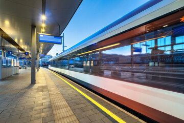 Wall Mural - high-speed passenger train in motion at the illuminated railway station at night. moving white moder