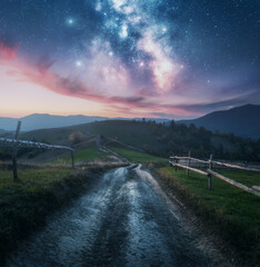 Wall Mural - milky way, rural road, fence, green hills in mountains at night