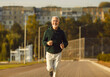 © Studio Romantic - Staying active after retirement. Happy joyful mature retired sportsman doing sports and running in stadium in morning. Caucasian gray-haired senior man in sportswear running and smiling at camera.
