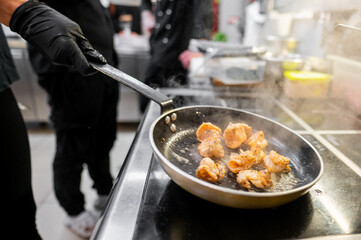 Wall Mural - Close-up of a frying pan on a stove, sautéing chunks of shrimp with steam rising. A person in black gloves holds the handle.