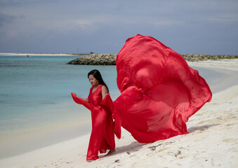 Wall Mural - Lady in red satin flying dress flowing at the beach