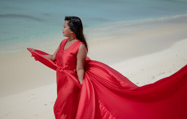 Wall Mural - Lady in red satin flying dress flowing at the beach