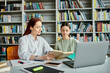 © LIGHTFIELD STUDIOS - a tutor and a teenage student, engrossed in after-school lessons at a library table with a laptop.