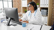 © Krakenimages.com - A hispanic woman doctor works attentively on a computer in a bright clinic office, wearing glasses and a stethoscope.