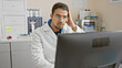 © Krakenimages.com - Worried young hispanic man in lab coat analyzing data on computer in hospital laboratory.