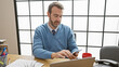 © Krakenimages.com - Mature man in office using smartphone with laptop, documents, and coffee on desk.