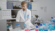 © Krakenimages.com - A focused man with beard and safety glasses analyzes data on a laptop in a modern laboratory setting.