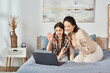 © LIGHTFIELD STUDIOS - mother and daughter, sharing a laptop while sitting on a cozy bed in a home setting.