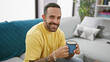 © Krakenimages.com - Smiling young hispanic man with a beard holding a coffee cup in a cozy living room.