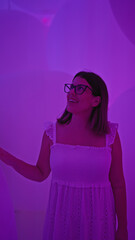 Wall Mural - Beautiful hispanic woman with glasses enjoys neon-lit balloon exhibit at futuristic, modern museum