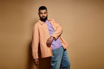 handsome african american man posing in fashionable attire against a vibrant brown backdrop.