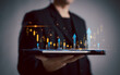 © Vatcharachai - Businessman holding a tablet with holographic financial growth charts and arrows. Represents stock market analysis, technology, and investment strategies.