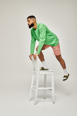 Wall Mural - African American man in green shirt standing on stool against vibrant backdrop.