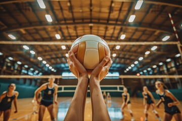 Close-up of hands holding volleyball in gymnasium with players in background, capturing the intensity and focus moments before the match begins.