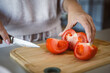 © Lana Milanovic - An unknown woman stand and cut tomato with knife on table at home