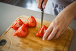 © Lana Milanovic - An unknown woman stand and cut tomato with knife on table at home