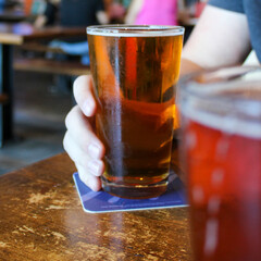 glass of amber colored beer on the table at restaurant with male hand holding around cup