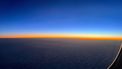 Wall Mural - A stunning view of the sunny sky from a plane window, with clouds forming intricate patterns below, creating a serene and expansive horizon.