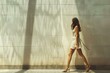 © anatolir - Stylish woman strides along a sundrenched urban sidewalk, casting a long shadow