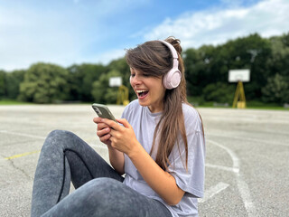 Young woman with headphones looking at her cell phone with surprised expression 
