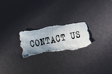 A torn piece of paper with the words Contact Us written on it, conveying a message for communication or assistance.