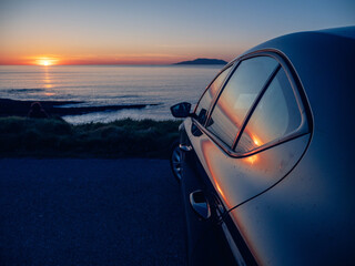Wall Mural - Dark car parked in a parking lot overlooking stunning nature scene with ocean, sunset sky and mountain in the background. Mullaghmore, Ireland. Irish landscape. Travel and tourism.